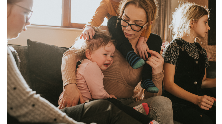 A busy single Mum of 4 comforts a crying toddler while surrounded by older children