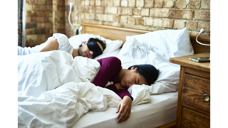 Woman asleep with hand on mattress and man wearing eye mask