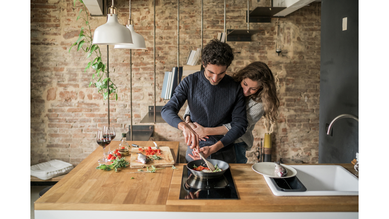 Young couple cooking fish cuisine at kitchen counter hob