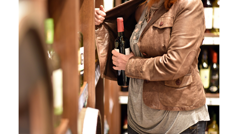 shoplifting - a woman steals a bottle of wine in a supermarket