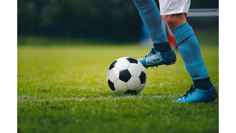 Close up of legs and feet of football player in blue socks and shoes running and dribbling with the ball. Soccer player running after the ball. Sports venue in the background