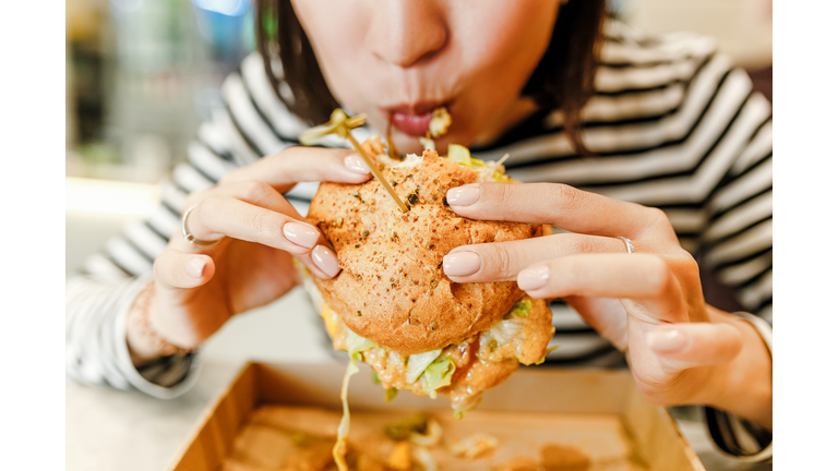 Woman eating a hamburger in modern fastfood cafe, lunch concept