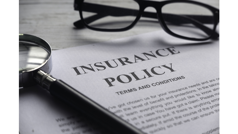 Selective focus of magnifying glass,glasses and Insurance Policy letter on a white wooden background.