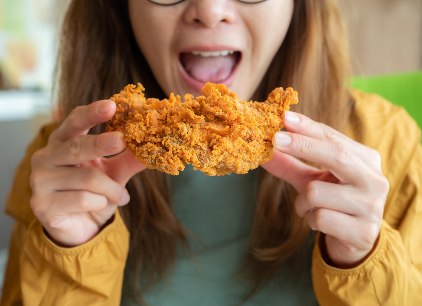 Cropped shot of young Asian woman open her mouth before eating a piece of crispy fried chicken.