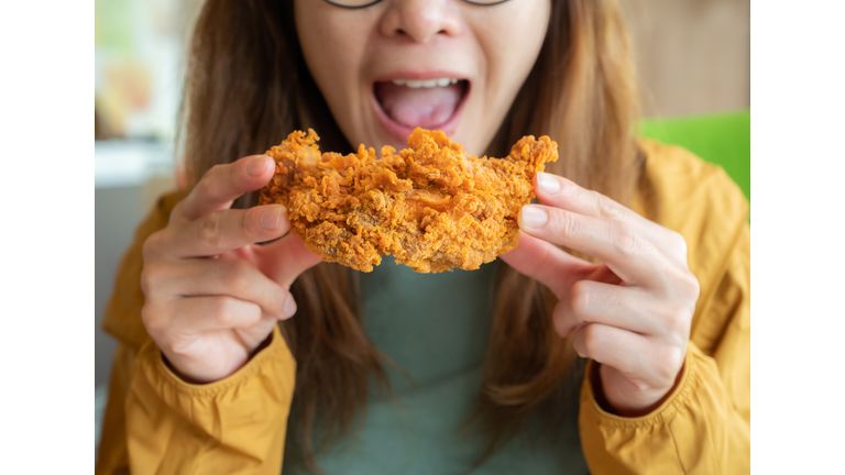 Cropped shot of young Asian woman open her mouth before eating a piece of crispy fried chicken.