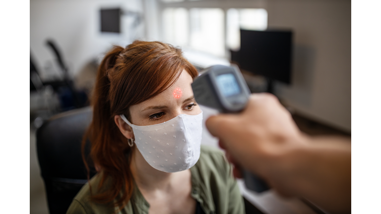 Businesswoman getting her temperature checked in office