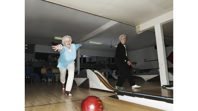 Mature woman throwing bowling ball down lane