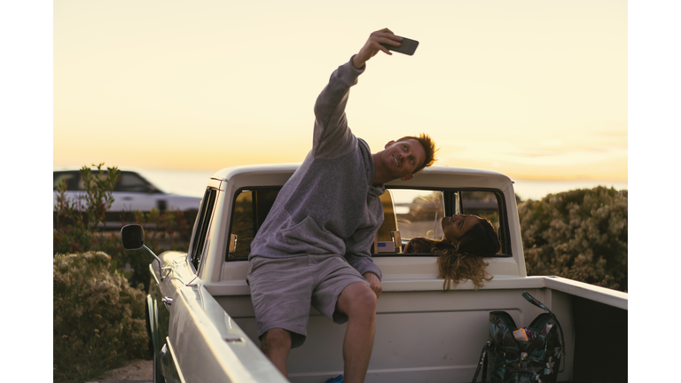 Man taking smartphone selfie with girlfriend in back of pickup truck at Newport Beach, California, USA