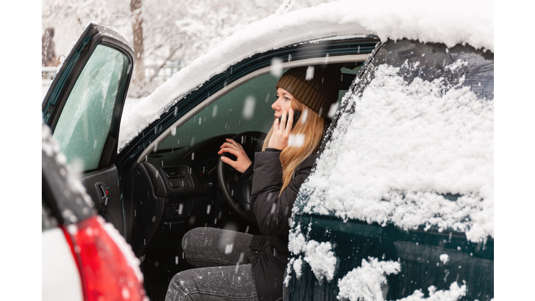 Young woman calling for help or assistance inside snow covered car. Engine start in frost. Breakdown services in the winter