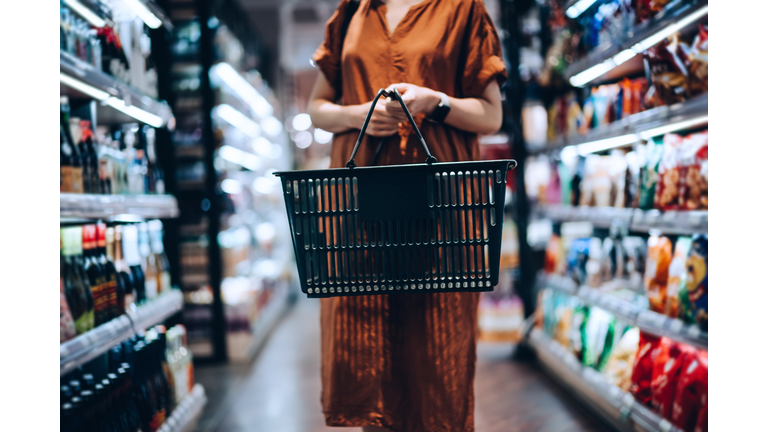 Cropped shot of young woman carrying a shopping basket, standing along the product aisle, grocery shopping for daily necessities in supermarket