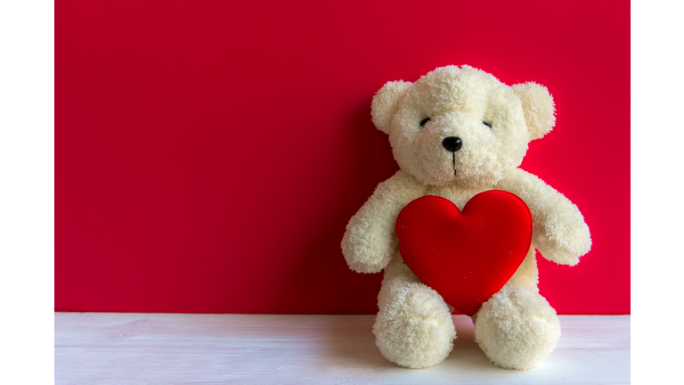 Cute teddy bear with red heart on old wood, copy space, red background. Valentine Concept