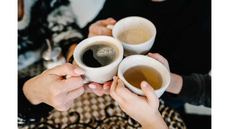 Hands hold the cups with coffee and tea in the morning. Happy mother, father and son having breakfast in the kitchen at home. Family, eating and people concept. Top view.