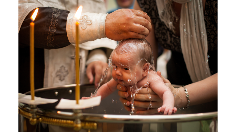 Newborn baby baptism in Holy water. baby holding mother's hands. Infant bathe in water. Baptism in the font
