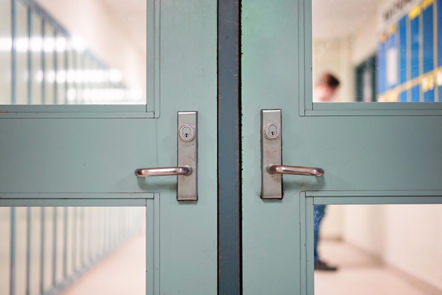 Student returning to school. School reopening by following social distancing rule after covid-19 pandemic lockdown. Locked door and handle see through blurred student lockers and student standing at background in high school or college.