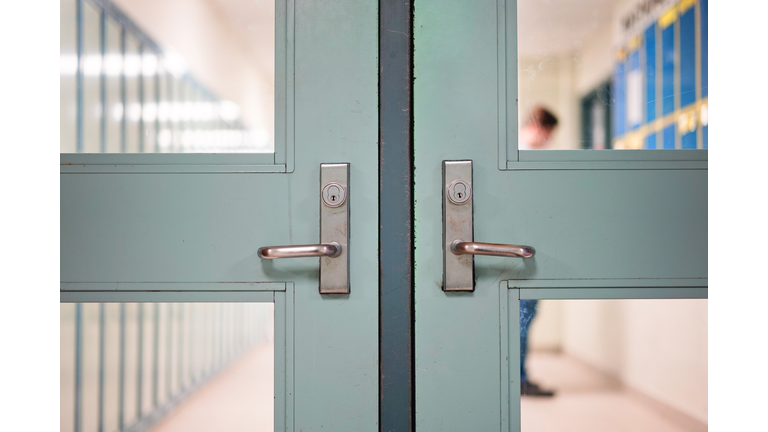 Student returning to school. School reopening by following social distancing rule after covid-19 pandemic lockdown. Locked door and handle see through blurred student lockers and student standing at background in high school or college.