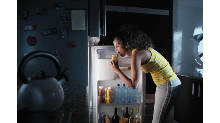 Side View Of Woman Eating Food While Standing By Refrigerator