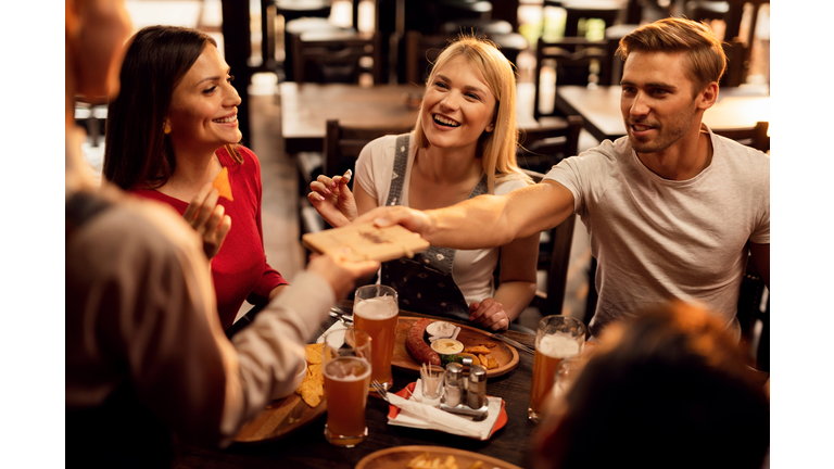 Group of happy friends paying restaurant check to a waiter.