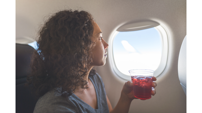 Young Eurasian woman enjoys a drink while seated by a window on an airplane