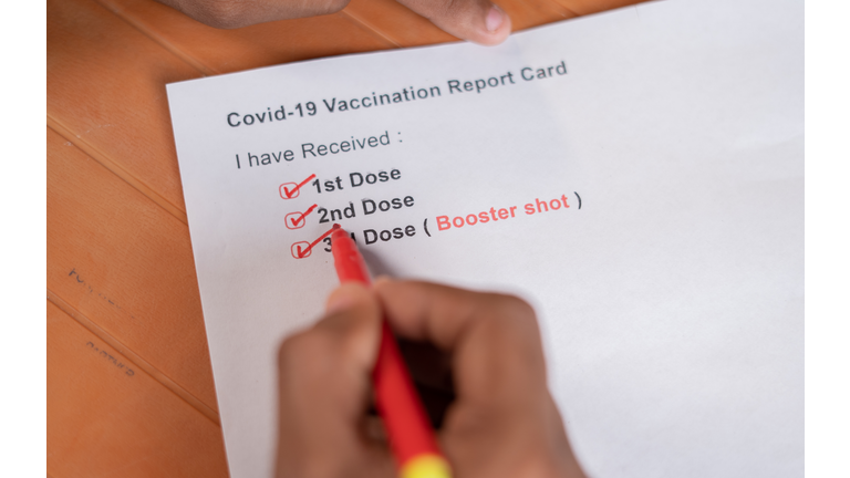 POV close up shot of hands checking Covid-19 vaccine report card and ticking 3rd or booster dose after vaccination