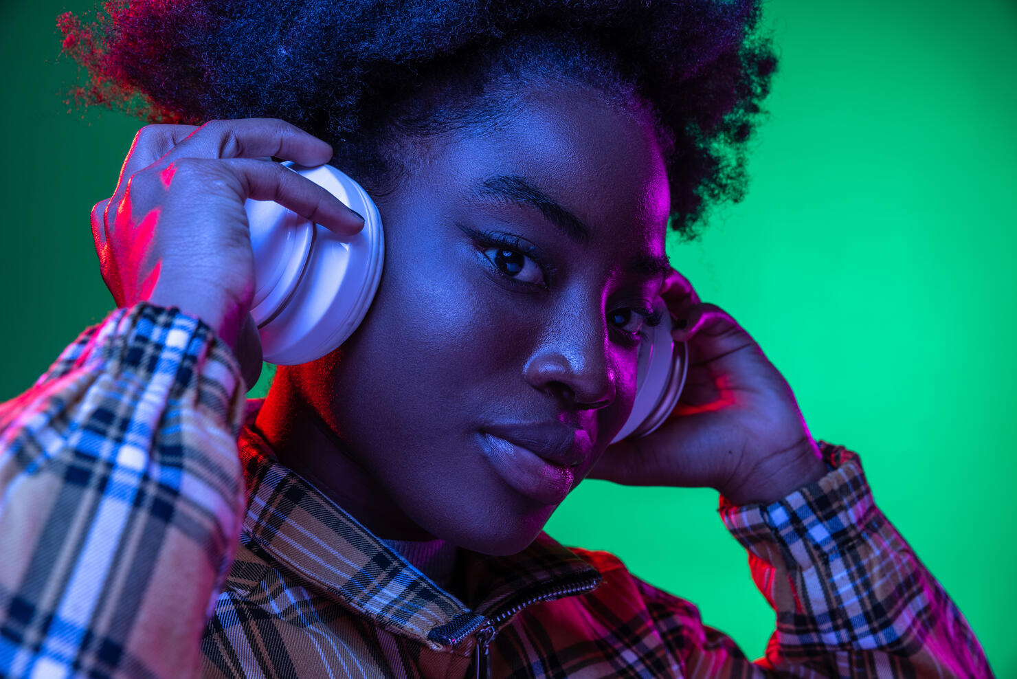 Close-up happy young girl, student listening to music in headphones isolated on dark green studio background in purple neon light.