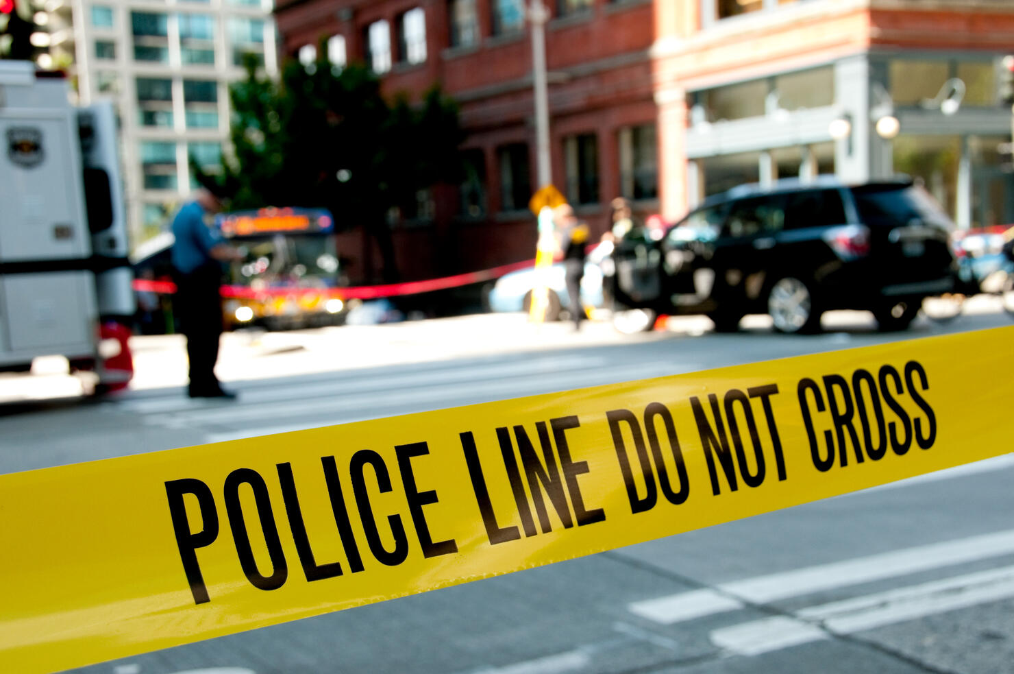Focus on police yellow crime scene tape with scene in rear