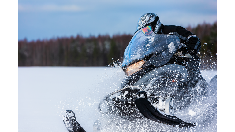 In deep powder snowdrift snowmobile rider driving fast.