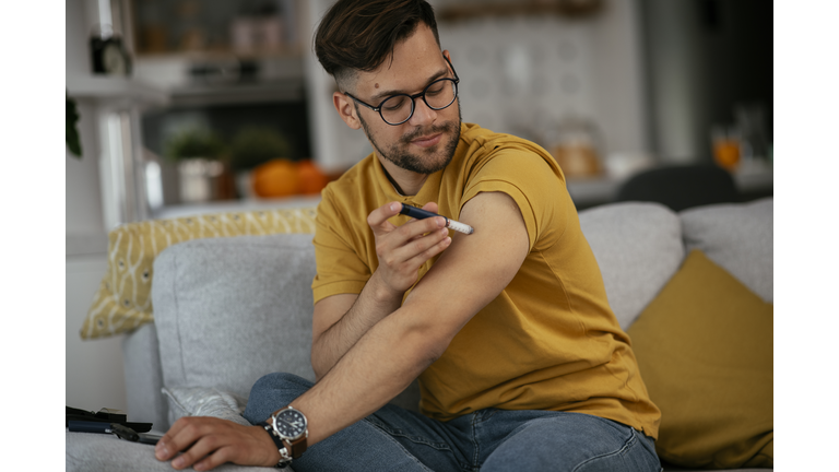 Young man giving himself an insulin shot at home.