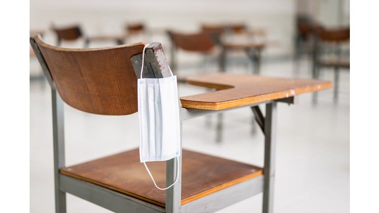 A used medical facemask hangs on a wood lecture chair in the empty classroom during the COVID-19 pandemic