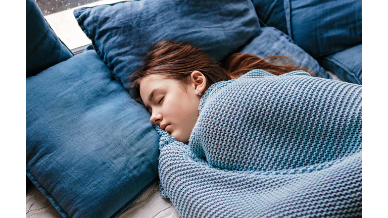 Young teenager girl sleeping snuggled in warm knitted blue blanket. Seasonal melancholy, apathy and winter blues. Cozy home.