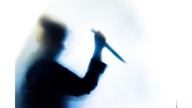 Violent silhouette of person wielding a knife behind frosted glass window