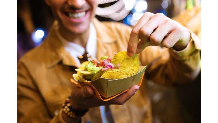 Attractive young man visiting eat market and eating nachos in the street.