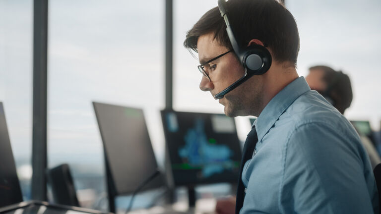 Male Air Traffic Controller with Headset Using Touchscreen Table Panel in Airport Tower. Office Room is Full of Computers with Navigation Screens, Airplane Flight Radar Data for the Team.