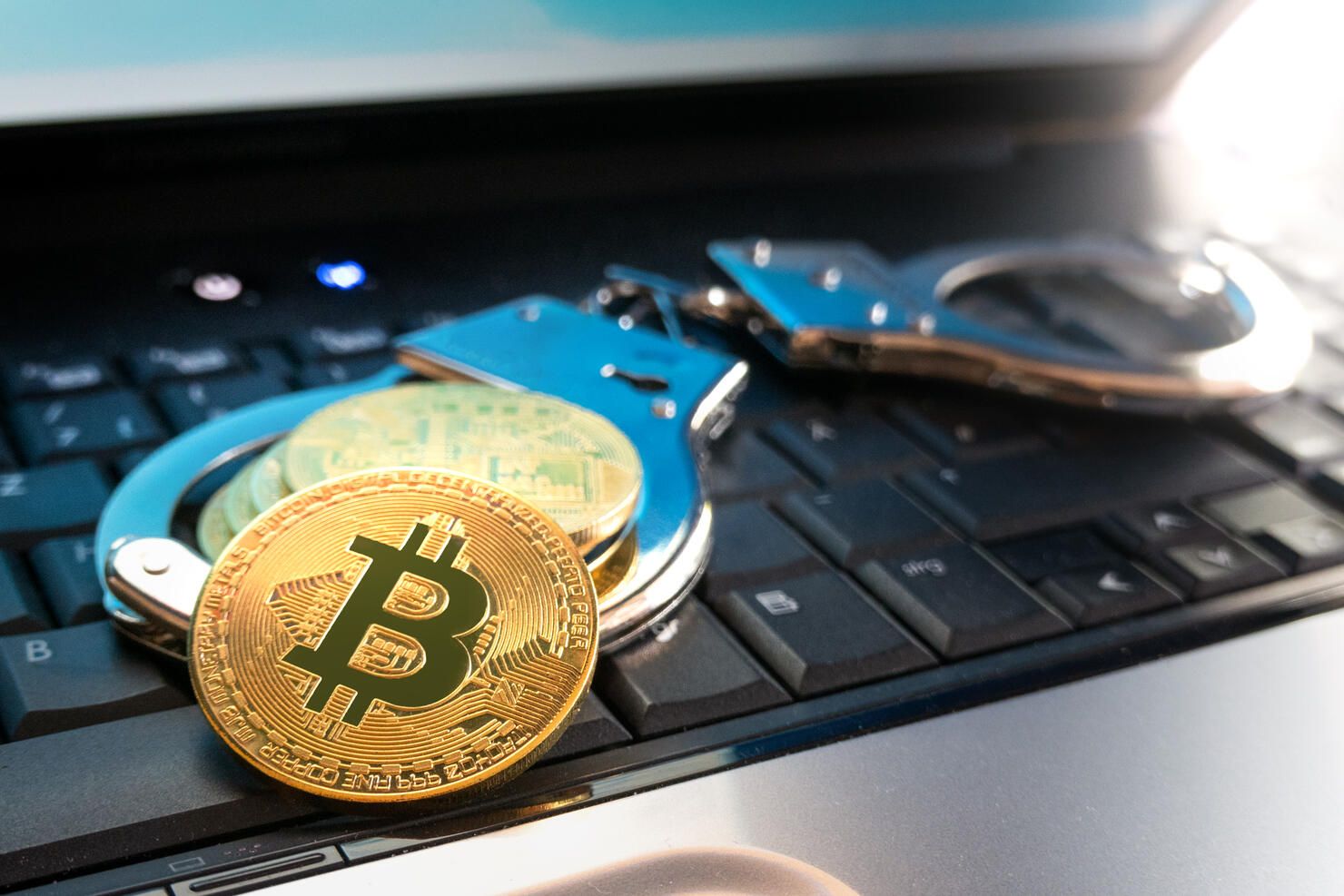 Bitcoin coins and handcuffs lie on the keyboard of the laptop.