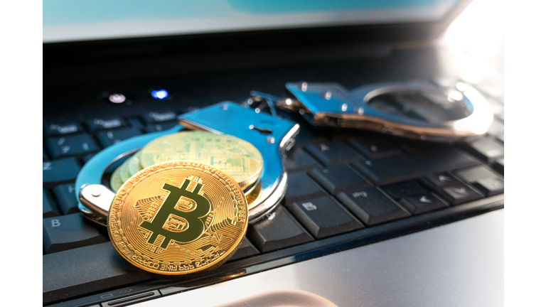 Bitcoin coins and handcuffs lie on the keyboard of the laptop.