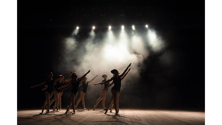 Ballet class on the stage of the theater with light and smoke. Children are engaged in classical exercise on stage.