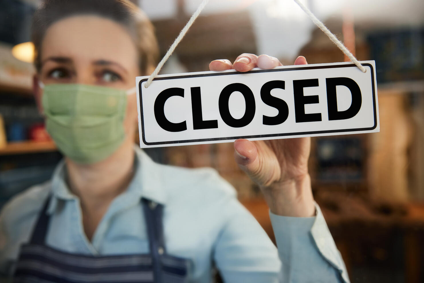 Female Owner Of Small Worried Business Wearing Face Mask Turning Round Closed Sign During Health Pandemic