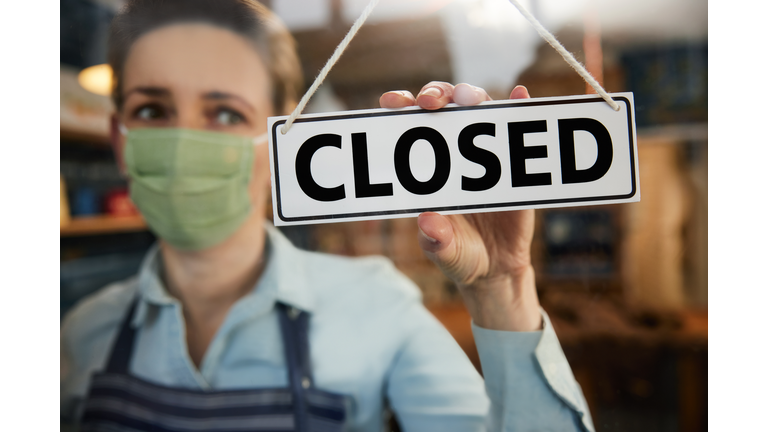 Female Owner Of Small Worried Business Wearing Face Mask Turning Round Closed Sign During Health Pandemic