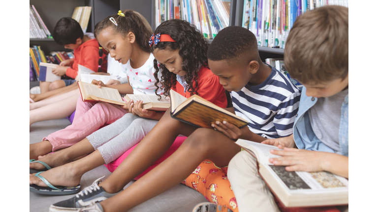 School kids sitting on cushions and studying over books in a library