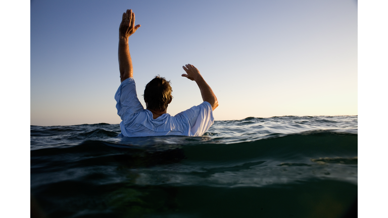 Man overboard in sea waving for help, rear view