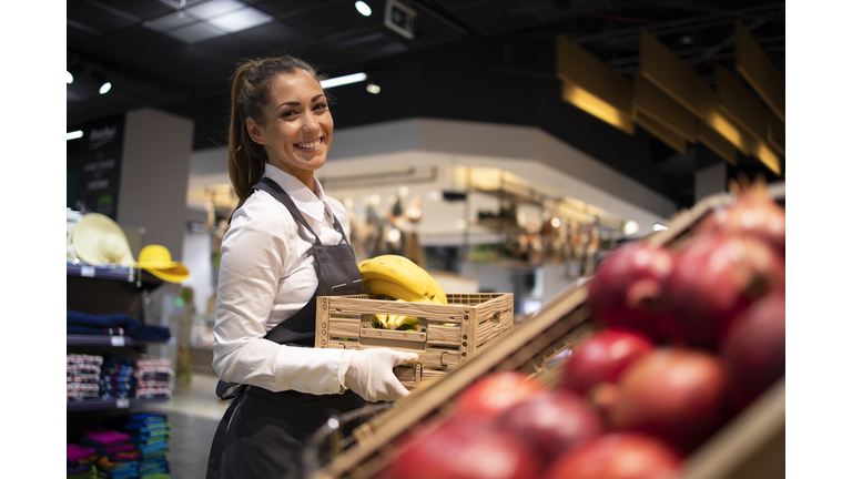 Working in grocery store. Supermarket worker supplying fruit department with food. Female worker holding crate with fruits.