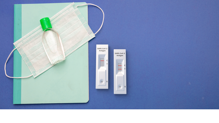 Coronavirus spread prevention measure at school. Rapid test, mask, disinfection gel and stationery on blue background,