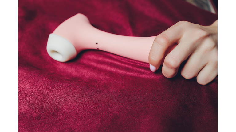 Woman in bedroom holding vibrator in hand.