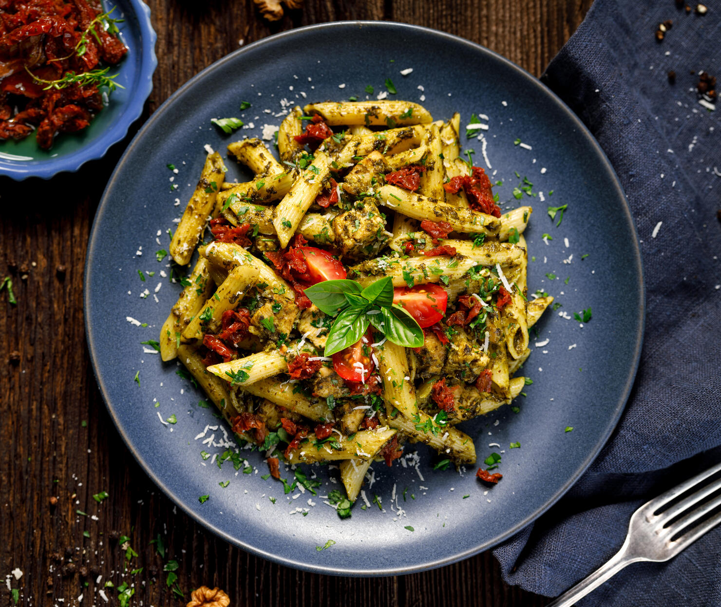 Penne pasta with spinach, sun dried tomatoes and chicken, sprinkled with parmesan cheese and fresh parsley  on a ceramic plate