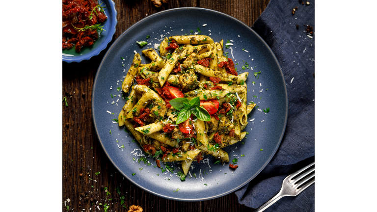 Penne pasta with spinach, sun dried tomatoes and chicken, sprinkled with parmesan cheese and fresh parsley  on a ceramic plate