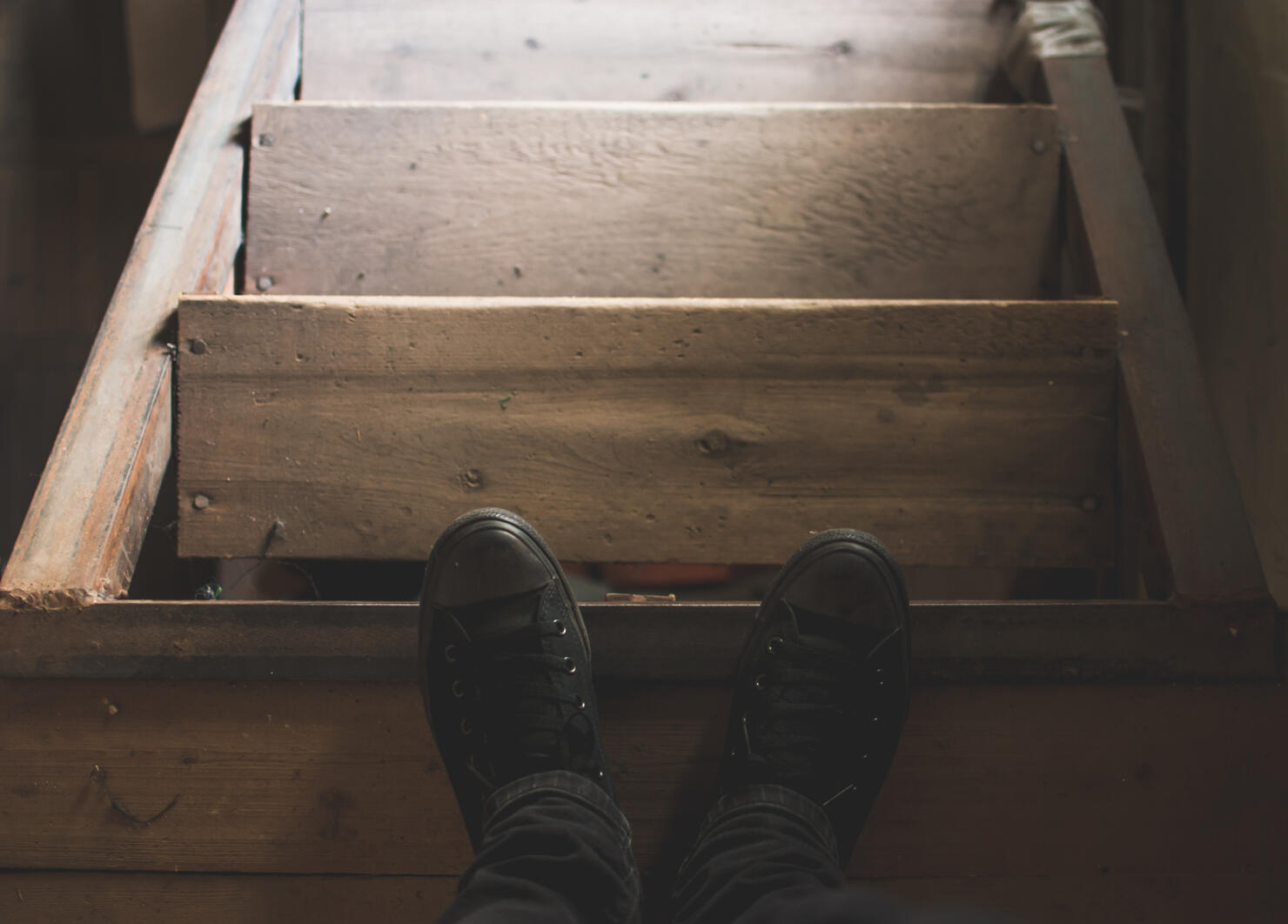 Man's black sneakers and old dusty loft wooden stairs
