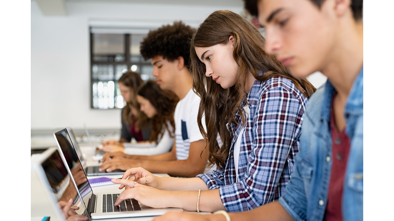 Group of high school students using laptop in classroom