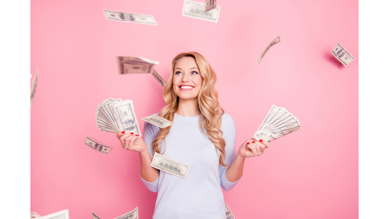 Portrait of pretty charming positive cute successful lucky cheerful girl standing under shower from money having a lot of money in hands isolated on pink background