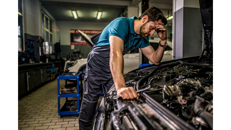 Worried mechanic examining engine problems in auto repair shop.