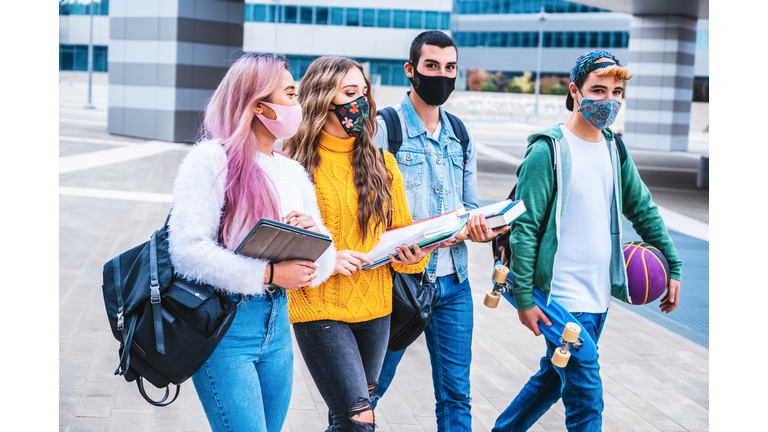 Happy interracial college friends walking In campus with face mask in covid-19 time - Concept about millennial enjoying spending time together outdoors