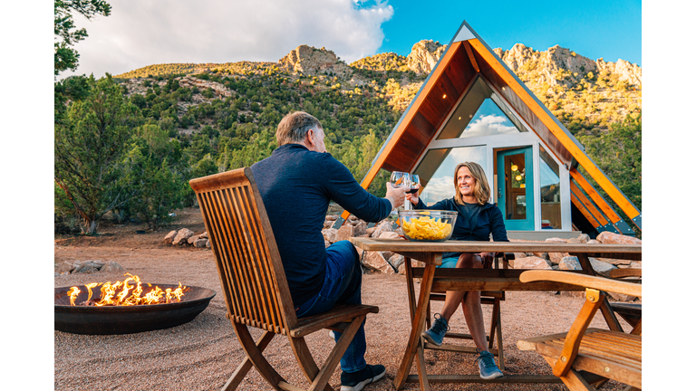 "Cheers!" Caucasian Couple Sharing a Celebratory Toast with Local Wine, Chips, and Salsa Together in a Xeriscaped Yard with a Cute Modern Xeriscaped Tiny Home in the Background